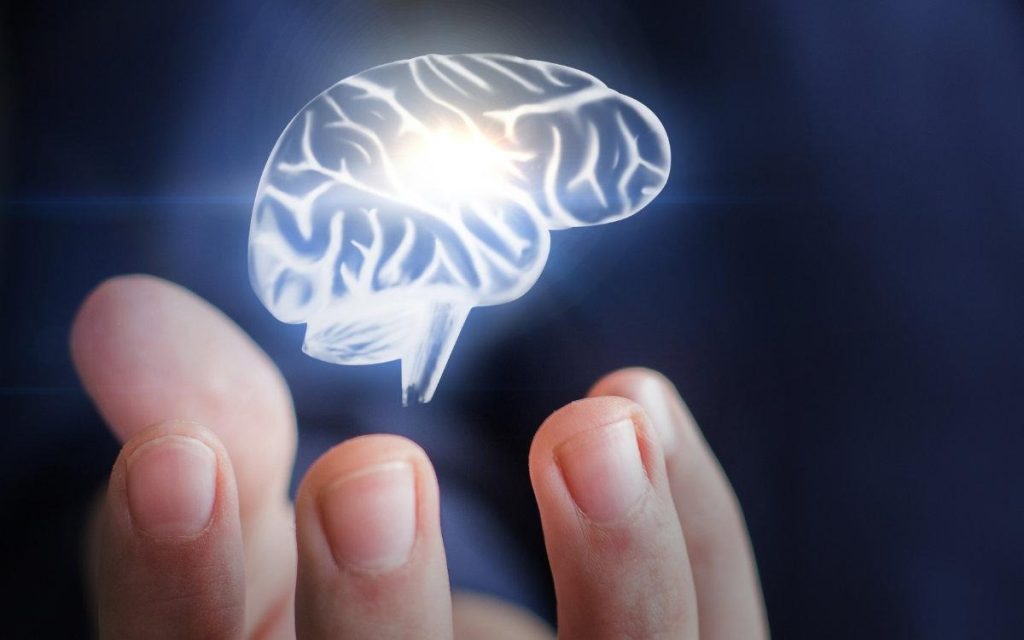 This image shows a futuristic concept of the human brain:
A 3D holographic brain is floating above a person’s fingers, giving a sense of technology and intelligence.
The brain is glowing with white and light blue highlights, emphasizing mental activity, thinking, and cognitive power.
The background is dark blue, which makes the glowing brain stand out more.
The hand under the brain suggests control, focus, or development of mental skills, implying that cognitive ability can be “handled” or “trained.”
The overall visual conveys a modern, tech-inspired idea of enhancing brain power and cognitive abilities.