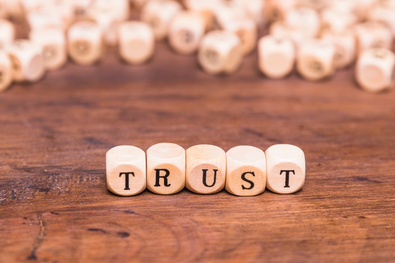 Close-up image of wooden letter blocks arranged to spell the word “TRUST” on a wooden surface, with similar blocks blurred in the background, symbolizing reliability, confidence, and strong foundational values.
