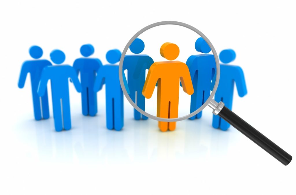 A magnifying glass highlighting one orange human figure among several blue figures, symbolizing candidate selection and recruitment focus.